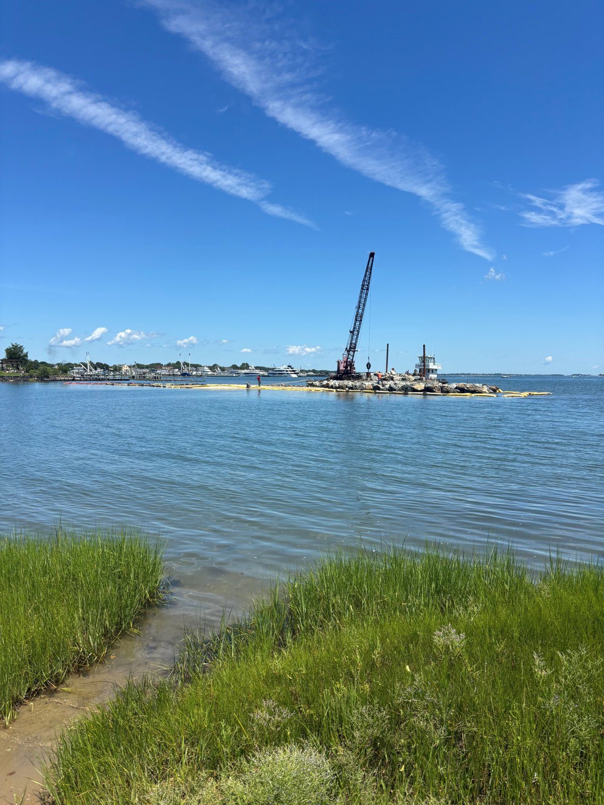 Crane barge placing stone at the Widow's Hole jetty, August 2026, seen from the preserve marsh