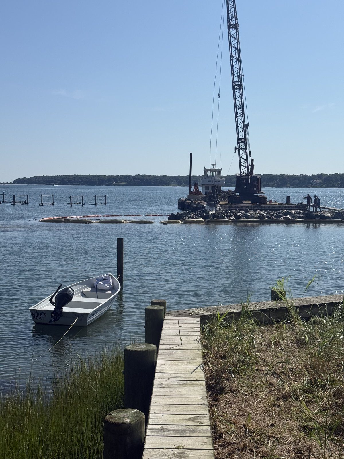 View down a wooden dock toward the crane barge at the Widow's Hole jetty, August 2026